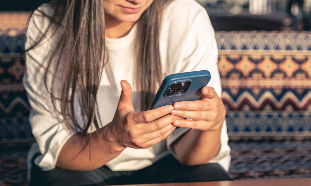 žena duge kose i u bijeloj majici u rukama drži mobitel